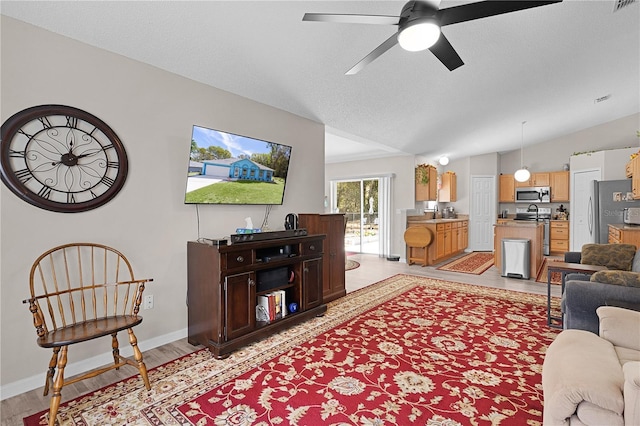 living area with light wood-type flooring, a ceiling fan, a textured ceiling, baseboards, and lofted ceiling