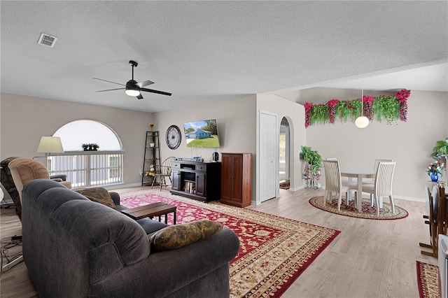 living area with arched walkways, light wood-style floors, a ceiling fan, and a textured ceiling