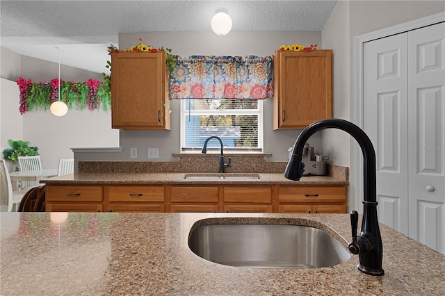 kitchen with light stone counters, brown cabinets, a textured ceiling, and a sink