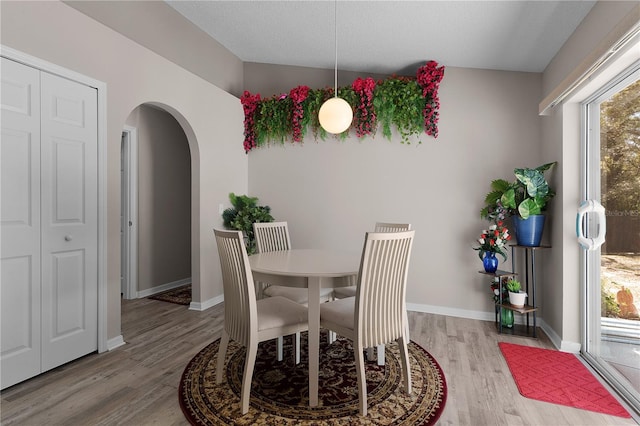 dining area featuring light wood-style flooring, baseboards, and arched walkways