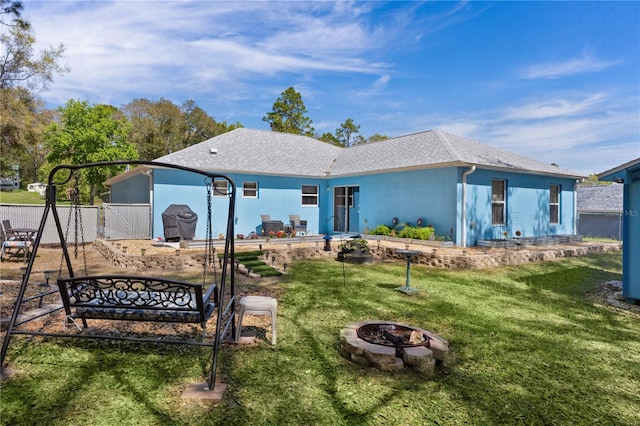 rear view of property with stucco siding, a lawn, an outdoor fire pit, and fence