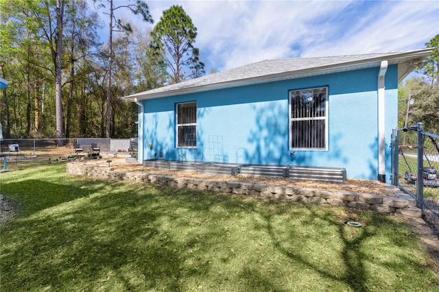 view of side of property featuring stucco siding, a yard, and fence