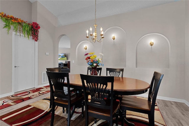 dining room featuring baseboards, arched walkways, an inviting chandelier, and wood finished floors