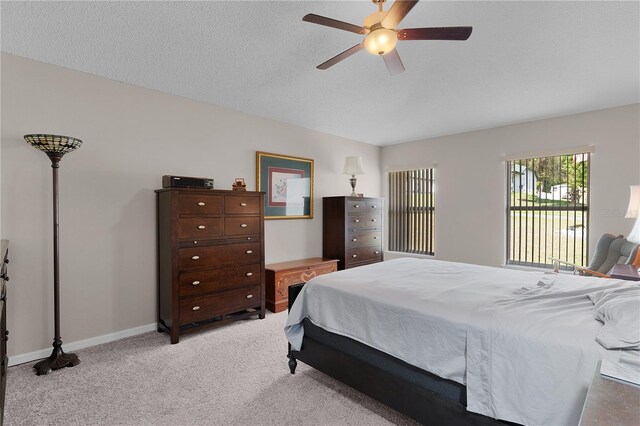 bedroom featuring baseboards, light carpet, a textured ceiling, and ceiling fan