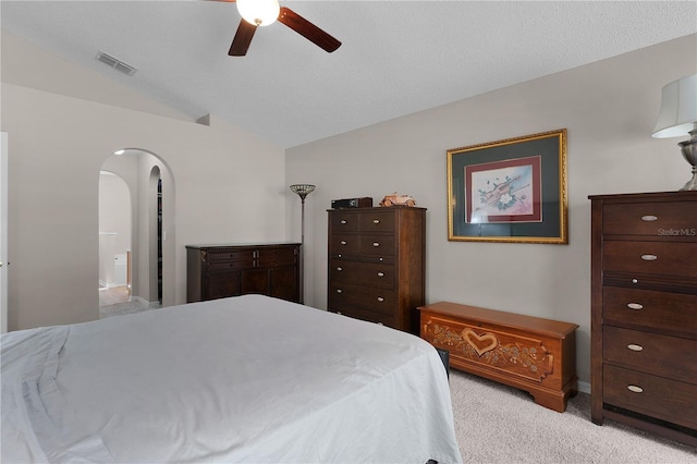 bedroom featuring visible vents, light carpet, ensuite bathroom, arched walkways, and vaulted ceiling