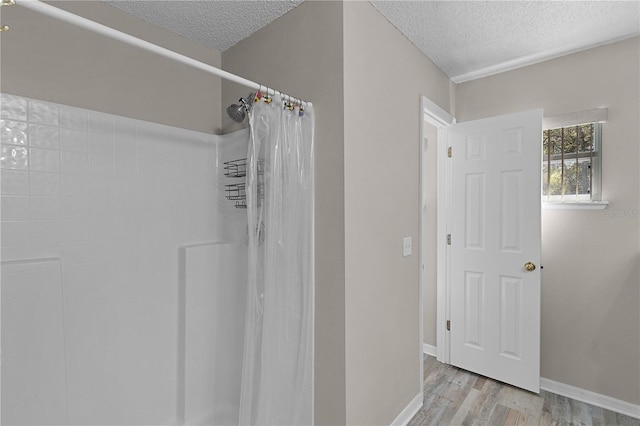 bathroom with a textured ceiling, a shower with shower curtain, baseboards, and wood finished floors