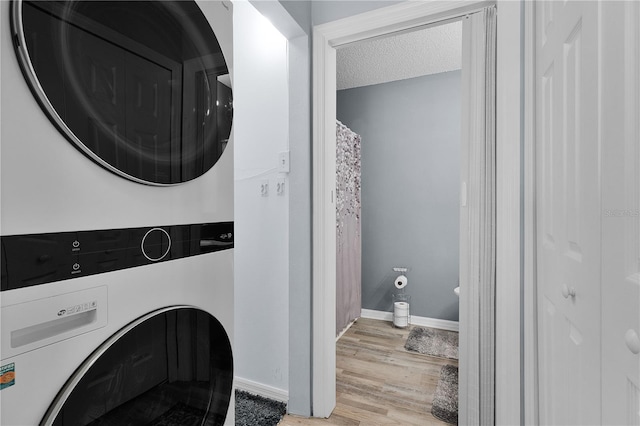 laundry room featuring stacked washer and clothes dryer, a textured ceiling, light wood-style floors, baseboards, and laundry area