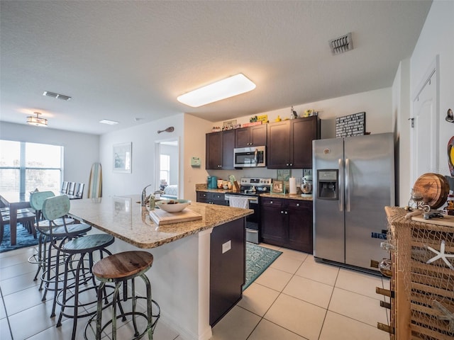 kitchen with appliances with stainless steel finishes, visible vents, a center island with sink, and dark brown cabinets