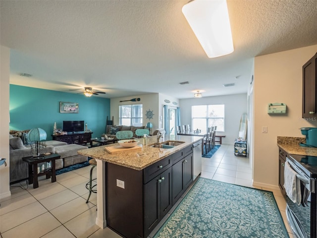 kitchen featuring open floor plan, light stone countertops, a kitchen island with sink, stainless steel appliances, and a sink