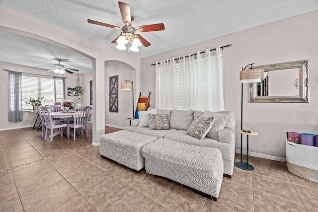 living room with a ceiling fan, a textured ceiling, tile patterned floors, arched walkways, and baseboards