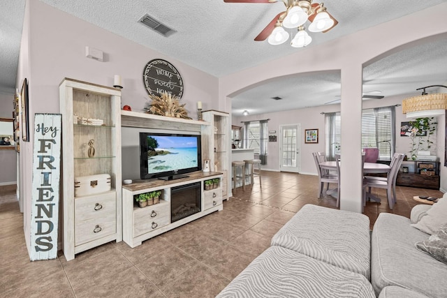 tiled living room with arched walkways, a textured ceiling, visible vents, and ceiling fan