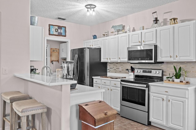 kitchen featuring white cabinets, stainless steel appliances, a textured ceiling, visible vents, and a breakfast bar
