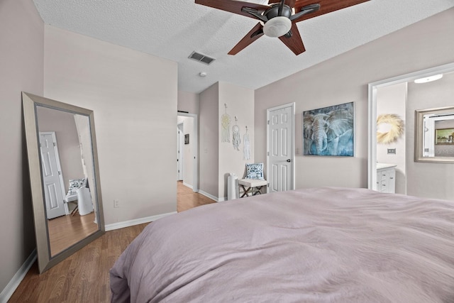 bedroom featuring wood finished floors, visible vents, ensuite bath, baseboards, and ceiling fan