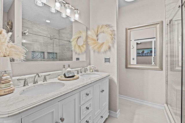 bathroom with a shower stall, baseboards, a sink, and double vanity