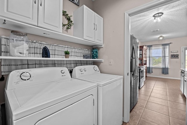 laundry area with light tile patterned floors, baseboards, separate washer and dryer, cabinet space, and a textured ceiling