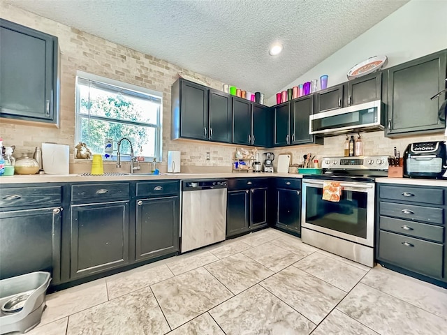 kitchen with vaulted ceiling, appliances with stainless steel finishes, sink, and backsplash