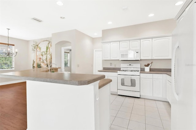 kitchen featuring white cabinetry, white appliances, decorative light fixtures, and a center island with sink