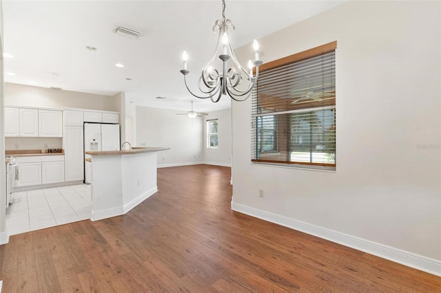 kitchen with decorative light fixtures, white cabinets, white refrigerator with ice dispenser, a center island with sink, and light wood-type flooring