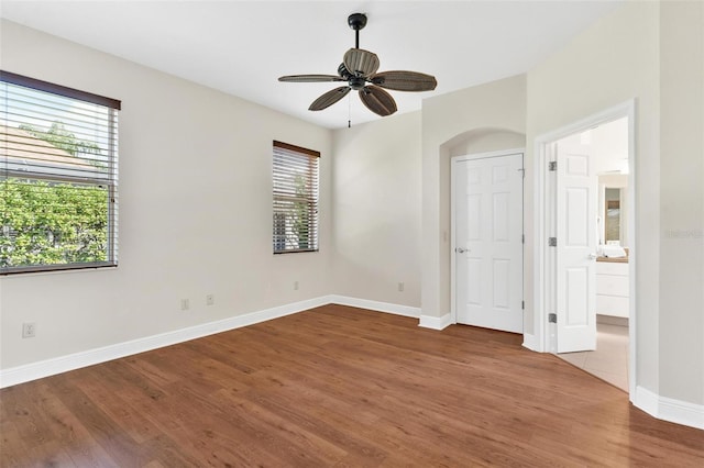 unfurnished bedroom featuring multiple windows, wood-type flooring, and ensuite bath