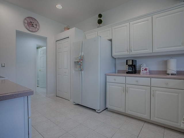 kitchen with white refrigerator with ice dispenser, light tile patterned floors, and white cabinets