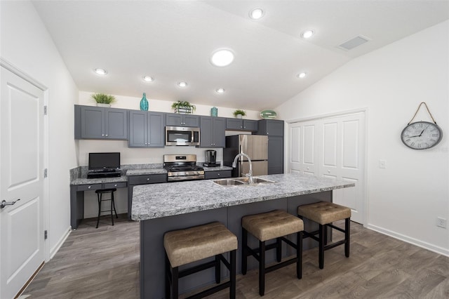 kitchen featuring an island with sink, appliances with stainless steel finishes, gray cabinets, a kitchen bar, and a sink