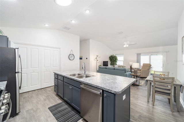 kitchen with lofted ceiling, a kitchen island with sink, stainless steel appliances, light countertops, and a sink