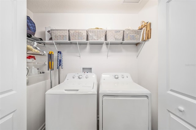 clothes washing area with laundry area, a textured ceiling, and washing machine and clothes dryer