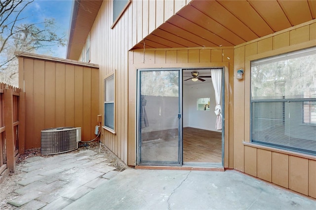 doorway to property with central AC unit, board and batten siding, a patio area, and fence