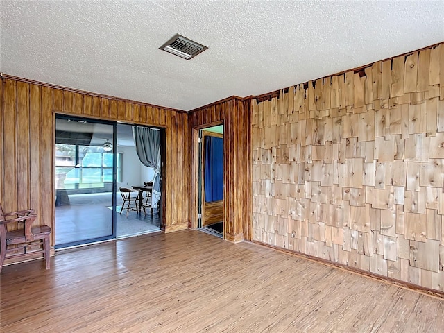empty room with a textured ceiling, wooden walls, ornamental molding, and wood-type flooring