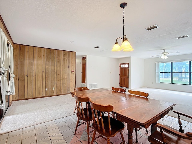 dining space featuring ceiling fan, light colored carpet, wooden walls, and a textured ceiling