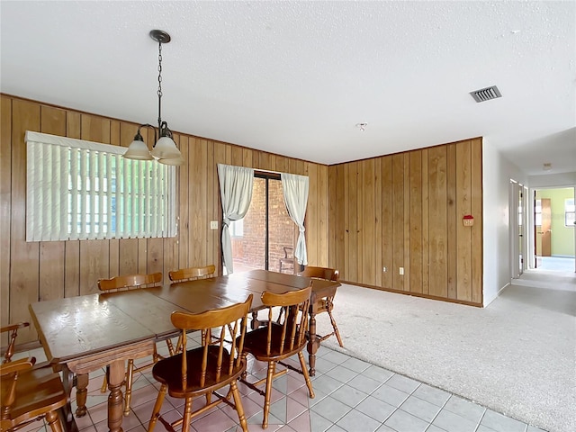 carpeted dining space with a wealth of natural light, a textured ceiling, and wood walls