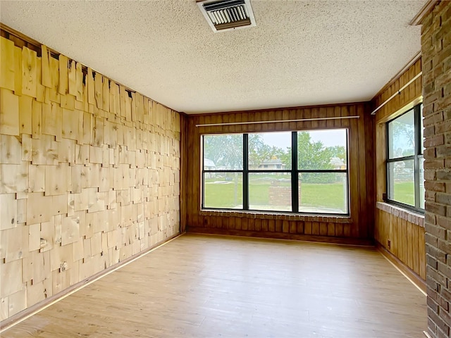 empty room featuring wood walls, a textured ceiling, and light hardwood / wood-style flooring