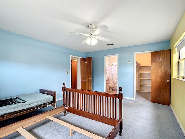 bedroom with ceiling fan, ensuite bathroom, light carpet, and a walk in closet