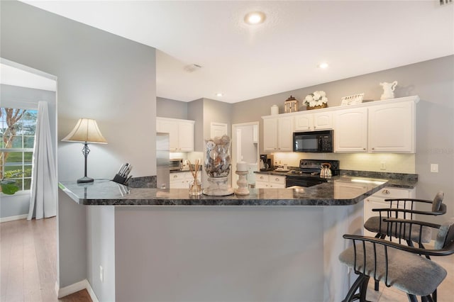 kitchen with black appliances, light hardwood / wood-style flooring, kitchen peninsula, decorative backsplash, and white cabinets