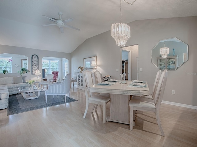 dining area featuring arched walkways, light wood finished floors, lofted ceiling, baseboards, and ceiling fan with notable chandelier