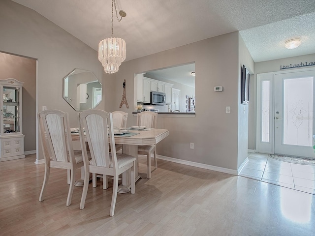 dining room with light wood finished floors, baseboards, a textured ceiling, and an inviting chandelier