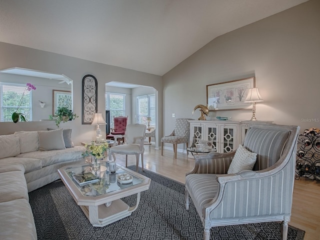 living room featuring a wealth of natural light, vaulted ceiling, arched walkways, and wood finished floors