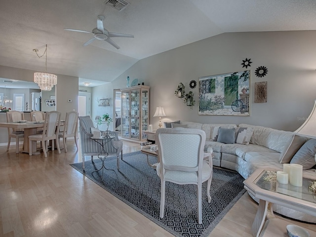 living area with lofted ceiling, ceiling fan with notable chandelier, light wood-type flooring, and visible vents