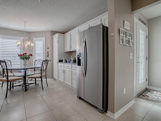 kitchen with light tile patterned floors, stainless steel fridge, white cabinetry, and light countertops