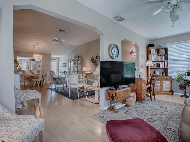 living area featuring visible vents, vaulted ceiling, light wood-style flooring, and ceiling fan with notable chandelier