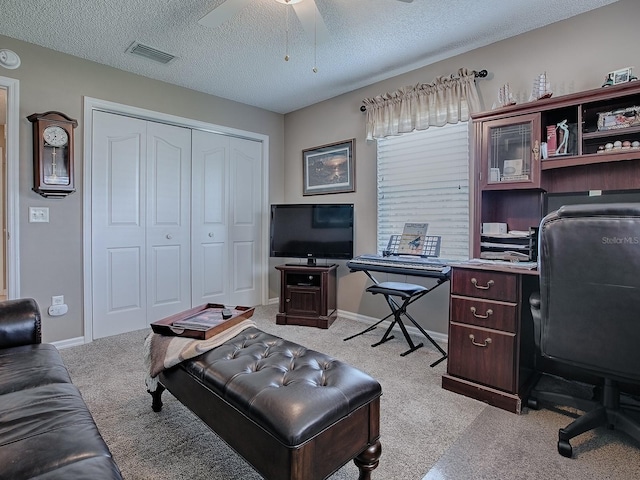 office area featuring light colored carpet, visible vents, a ceiling fan, a textured ceiling, and baseboards