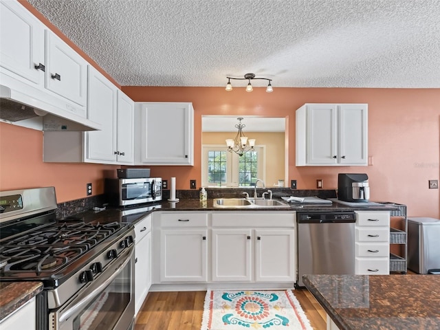 kitchen with sink, white cabinetry, decorative light fixtures, appliances with stainless steel finishes, and dark stone counters