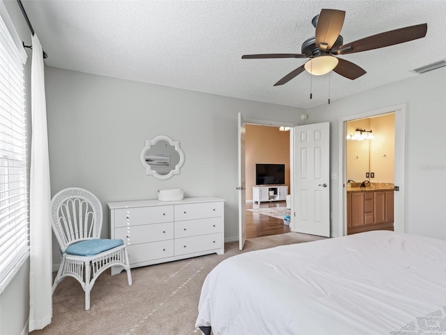 bedroom with ceiling fan, connected bathroom, light colored carpet, and a textured ceiling