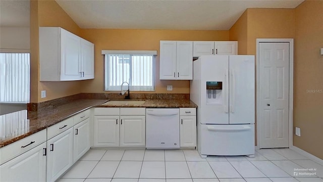 kitchen featuring sink, dark stone countertops, light tile patterned floors, white appliances, and white cabinets