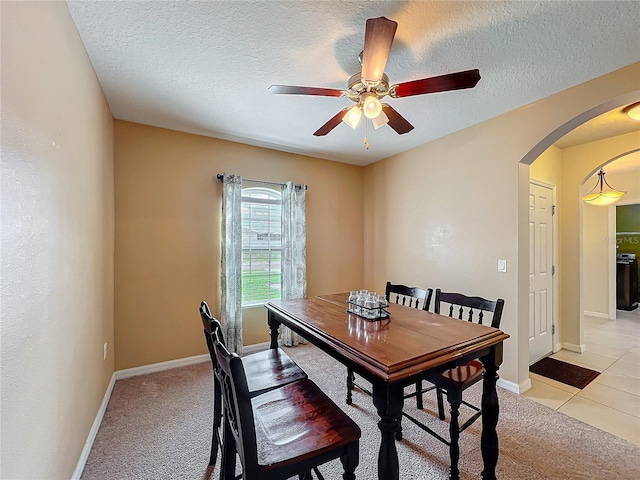 dining area with baseboards, arched walkways, light colored carpet, ceiling fan, and a textured ceiling