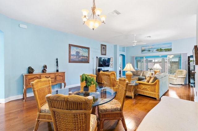 dining space featuring arched walkways, ceiling fan with notable chandelier, wood finished floors, visible vents, and baseboards