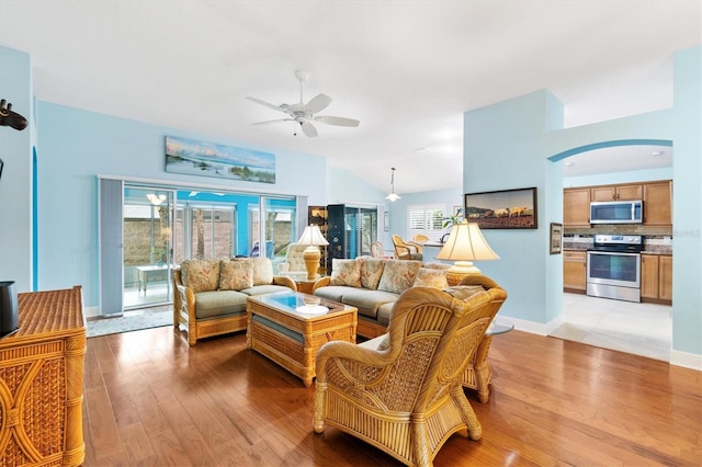 living room with baseboards, arched walkways, lofted ceiling, ceiling fan, and light wood-style floors