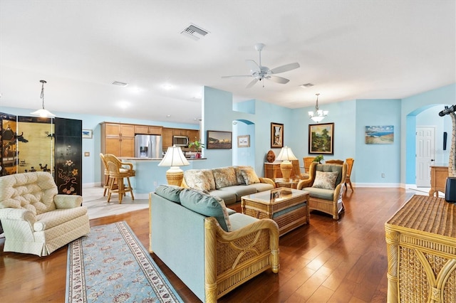 living room with arched walkways, a ceiling fan, visible vents, baseboards, and dark wood-style floors