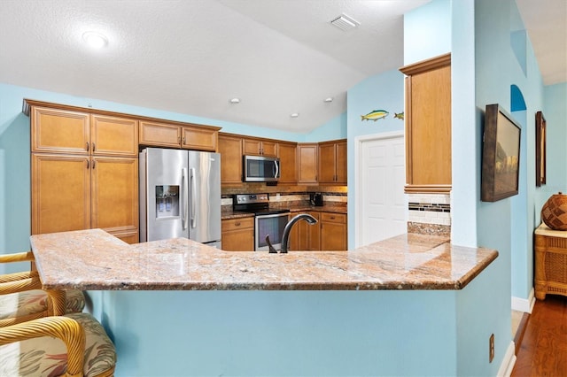 kitchen featuring a kitchen breakfast bar, a peninsula, light stone counters, and stainless steel appliances