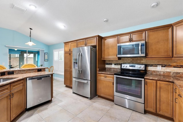 kitchen featuring stainless steel appliances, vaulted ceiling, hanging light fixtures, brown cabinets, and dark stone countertops